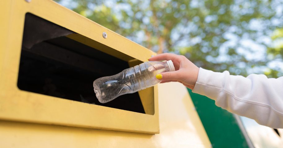 Kobieta wrzuca plastikową butelkę do pojemnika. Dlaczego warto segregować śmieci i jak robić to dobrze